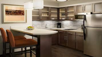 A modern kitchen with a stainless steel refrigerator, a coffee maker, and a bowl of fruit on the counter.