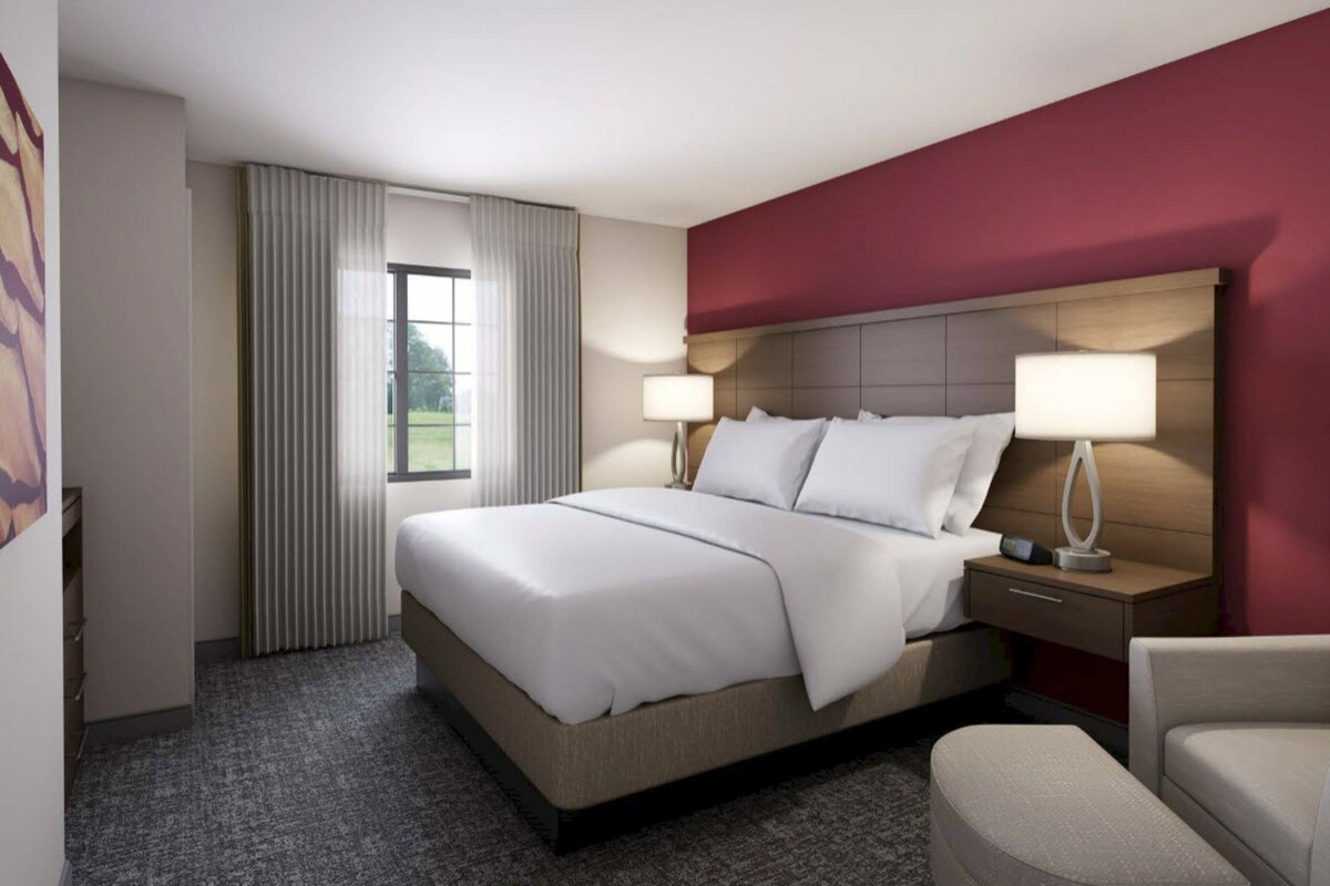 A hotel room with a large bed, two bedside tables with lamps, a chair, and a window with curtains.