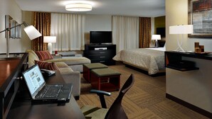 Ein Hotelzimmer mit Bett, Schreibtisch, Laptop, Fernseher und einer Sitzecke.