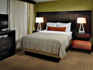 A hotel room with a bed, two bedside tables with lamps, a TV on a dresser, and a carpeted floor. - Staybridge Suites Lafayette by IHG (Lafayette)