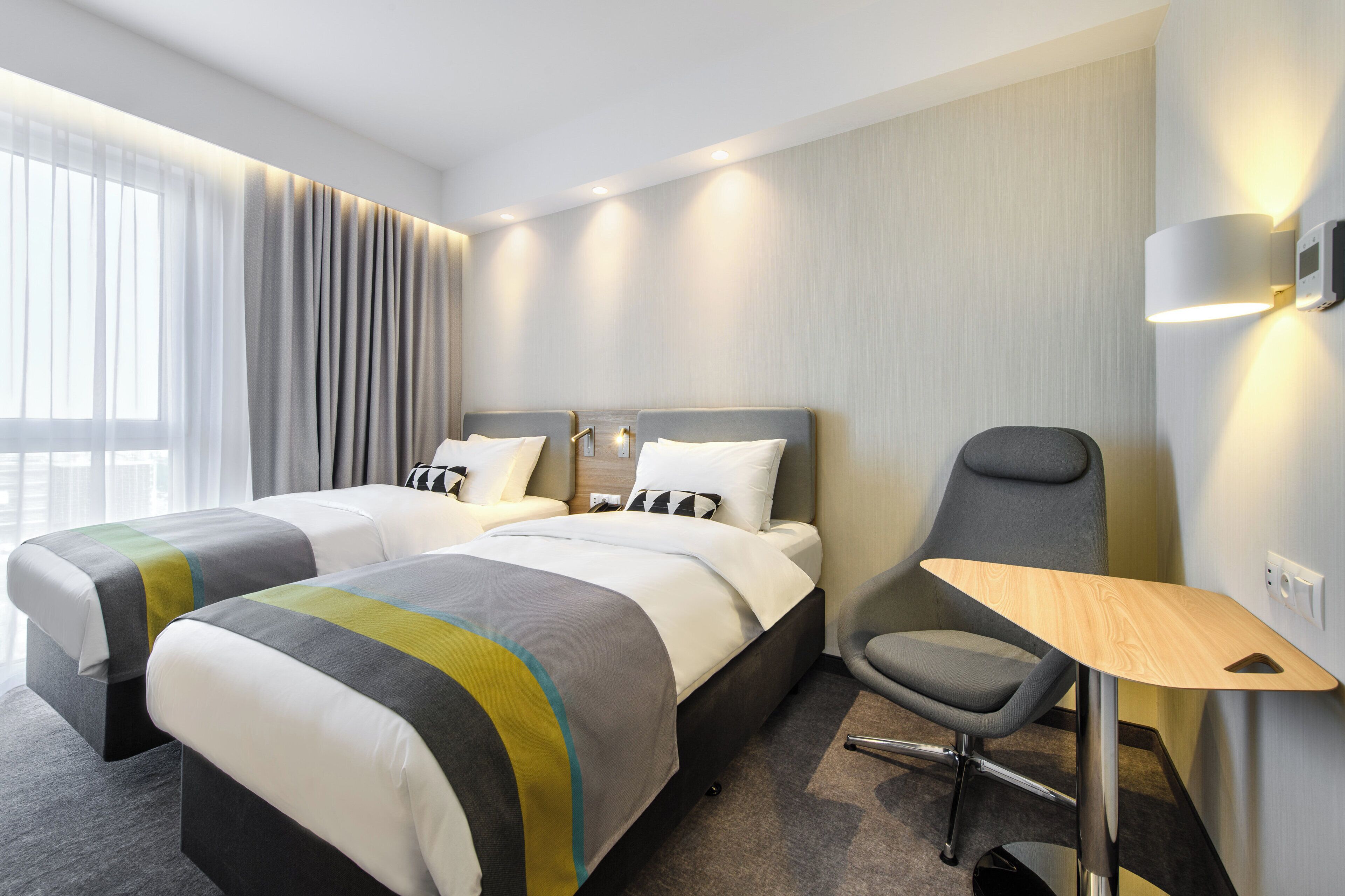 A hotel room with two beds, a desk, a chair, and a window with curtains.