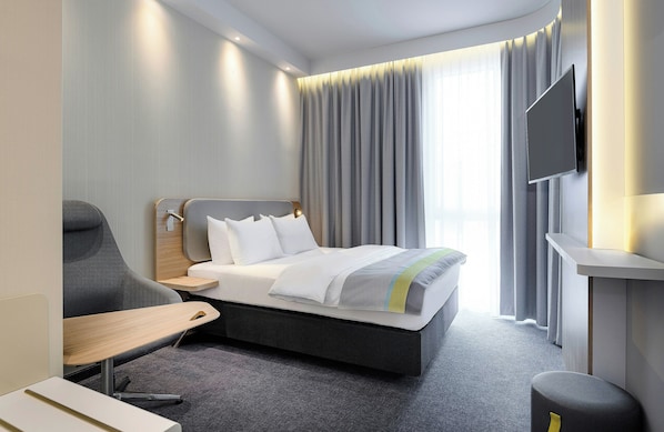 A modern hotel room with a bed, a desk, a chair, a TV, and curtains. - Leonardo Smart Hotel Regensburg (Regensburg)
