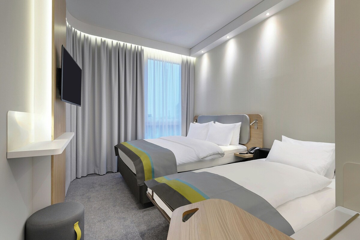 Une chambre d’hôtel avec un lit, des tables de chevet, une télévision et une fenêtre avec des rideaux.
