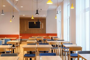A modern dining area with wooden tables and chairs, a large screen, and pendant lighting. - Holiday Inn Express Regensburg by IHG (Regensburg)