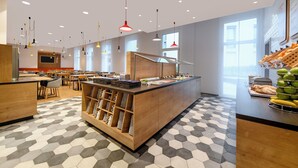 A modern cafe with a central counter, hexagonal patterned floor, and various seating arrangements. - Holiday Inn Express Regensburg by IHG (Regensburg)