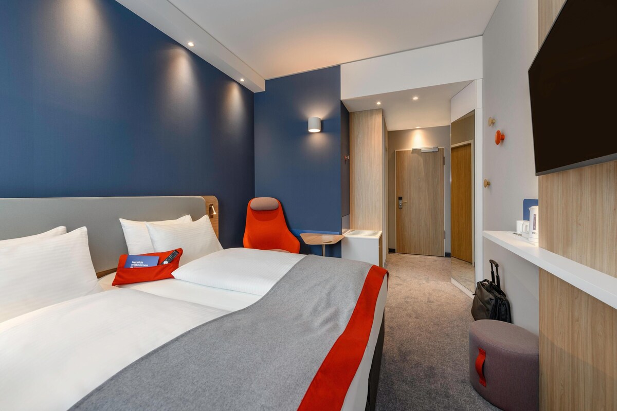 A hotel room with a bed, a desk, a chair, and a small seating area.