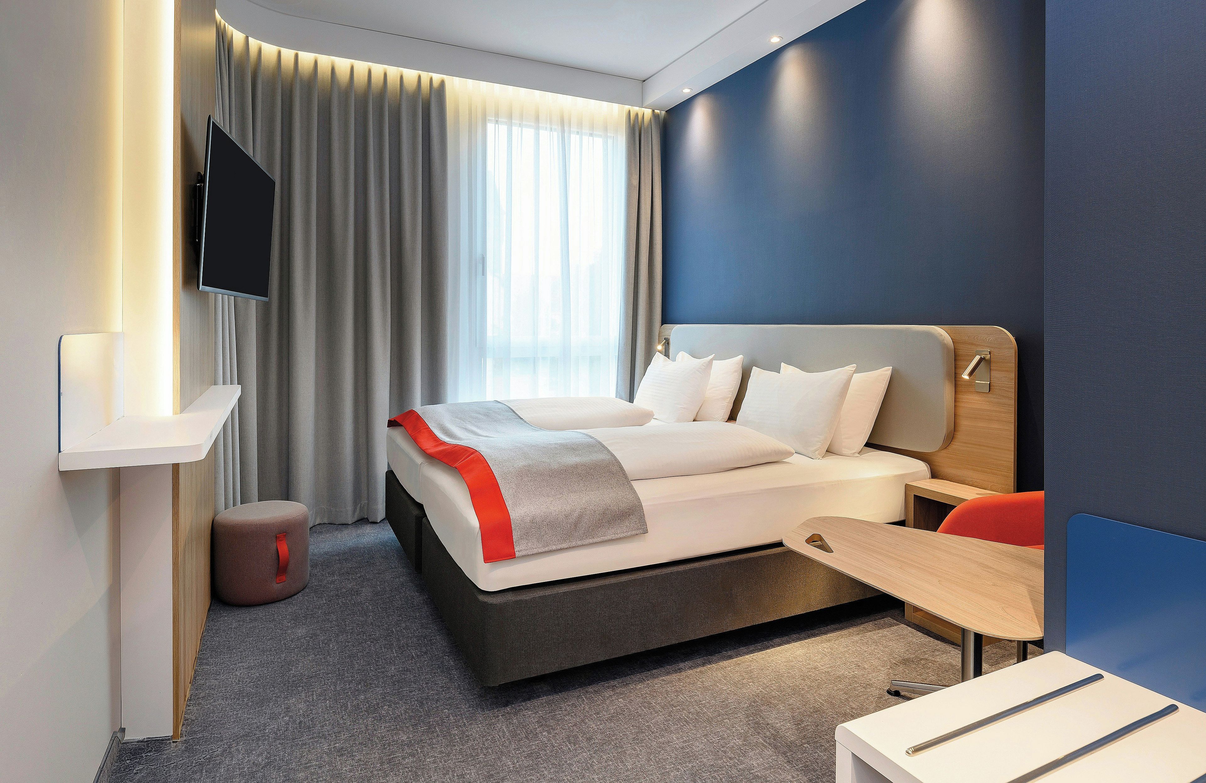 Una habitación de hotel moderna con cama, televisión, escritorio y silla.