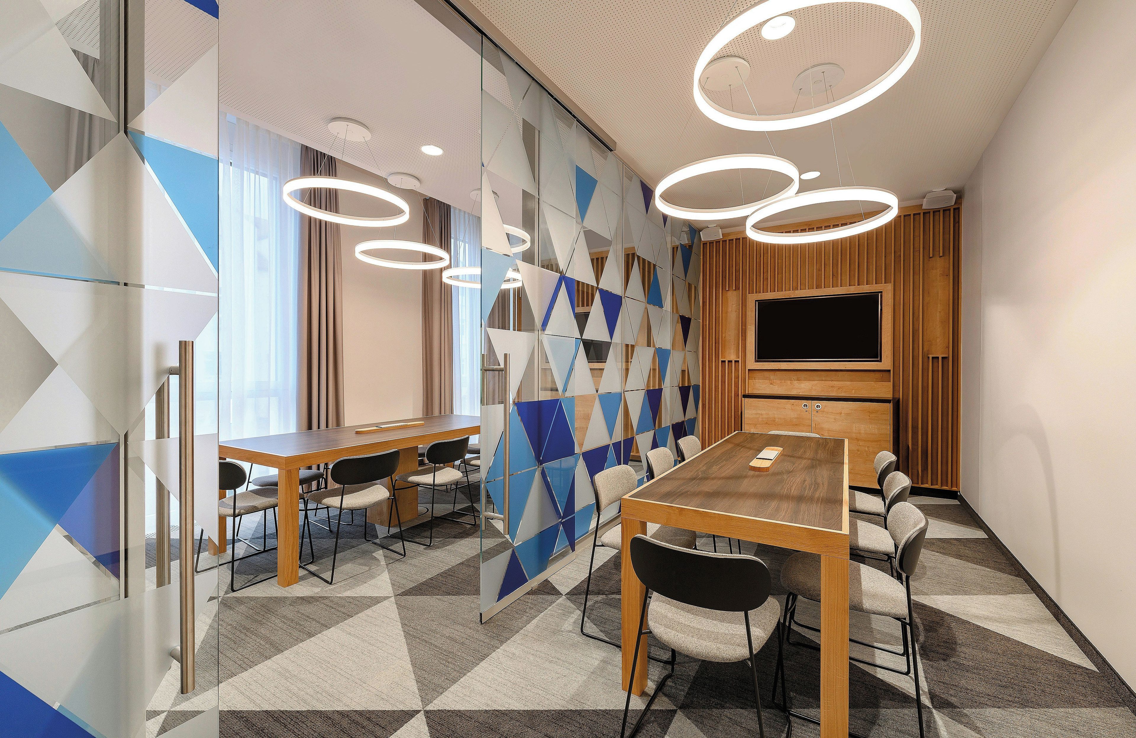 Una sala de conferencias moderna con una gran mesa, sillas, un televisor y paredes con un diseño geométrico.