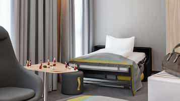 A hotel room with a bed, a small table with a board game, a chair, and a suitcase.