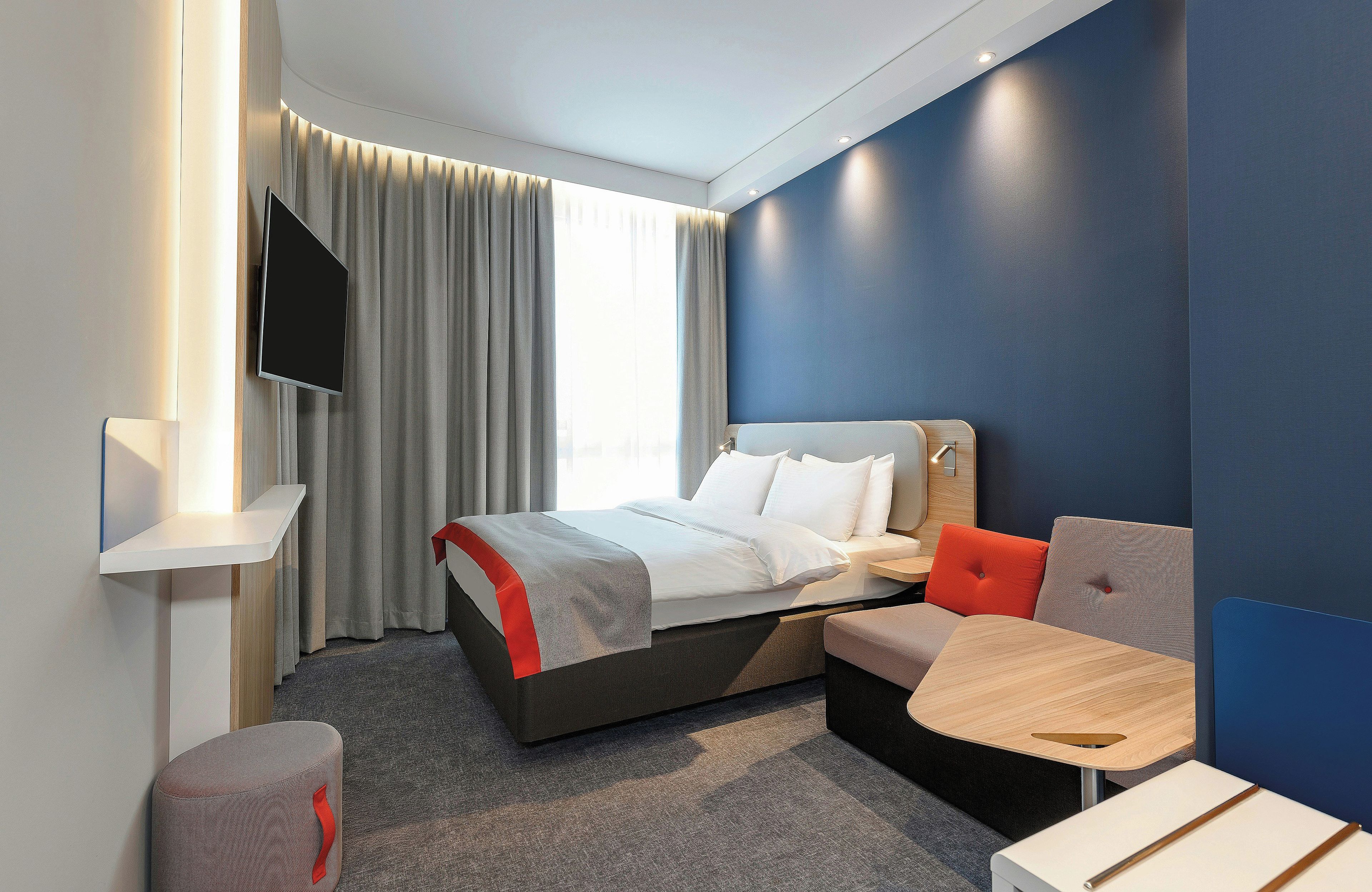 Habitació d'hotel moderna amb un llit, zona de seients, televisió de pantalla plana i una finestra amb cortines.
