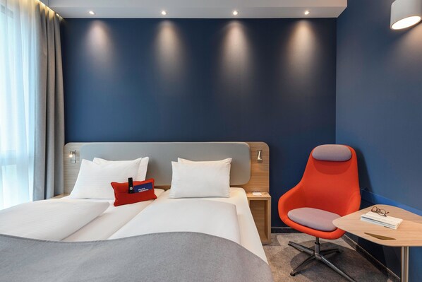 A hotel room with a bed, a nightstand, a red chair, and a small table. - Holiday Inn Express Regensburg by IHG (Regensburg)