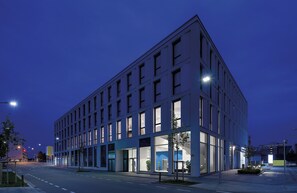 Un bâtiment moderne à la façade plate, doté de grandes fenêtres et d’un design épuré et géométrique.