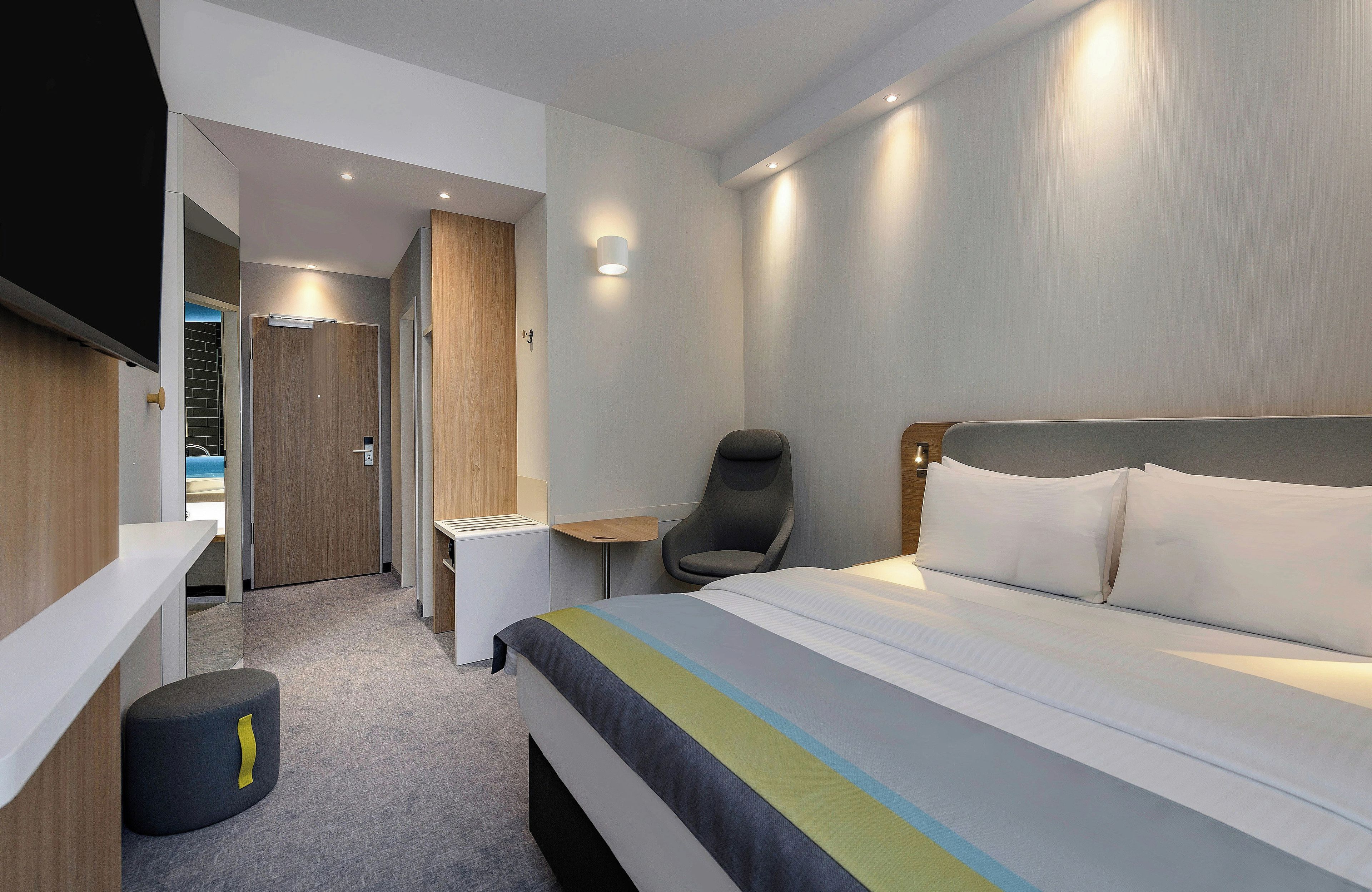 A modern hotel room with a bed, a desk, a chair, and a TV.
