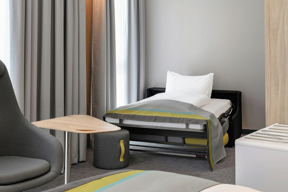 Une chambre d’hôtel avec un lit, une chaise, une petite table et une table de chevet.