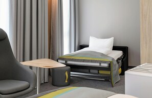 A hotel room with a bed, a chair, a small table, and a bedside table. - Leonardo Smart Hotel Regensburg (Regensburg)