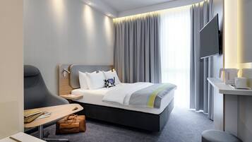 Una habitación de hotel moderna con una cama, un escritorio, una silla, un televisor y una ventana con cortinas.