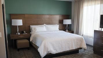 A hotel room with a large bed, two bedside tables with lamps, a nightstand, a dresser, and a window with curtains.