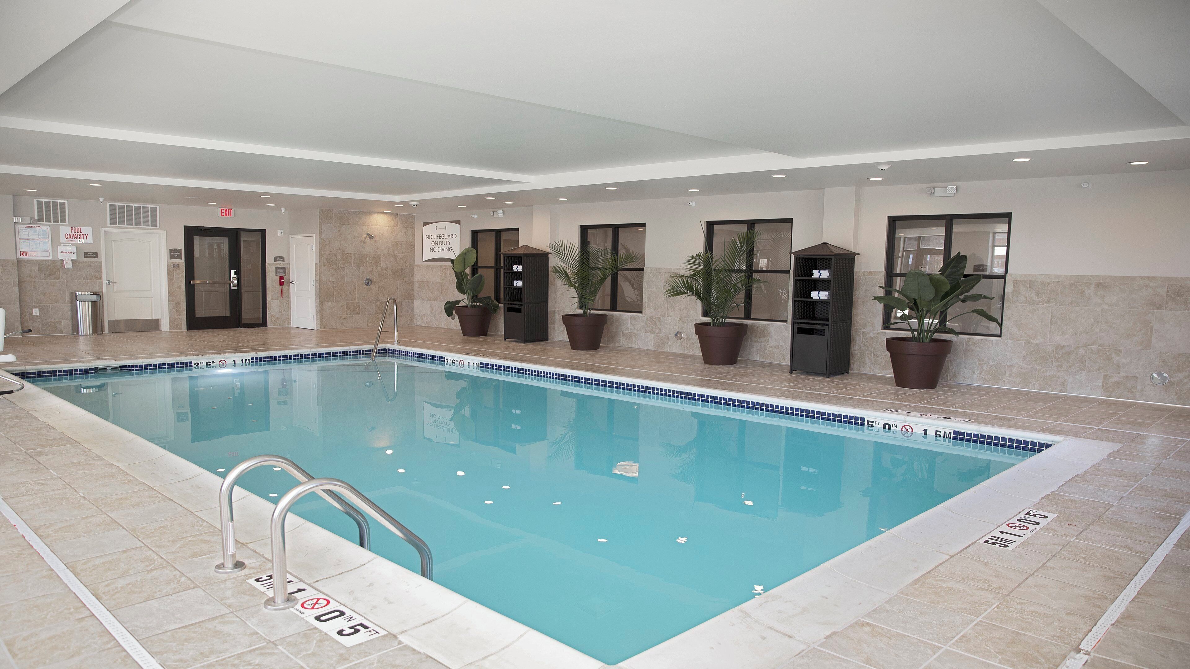 Una piscina interior con agua cristalina, bordes de azulejos y una escalera de metal.