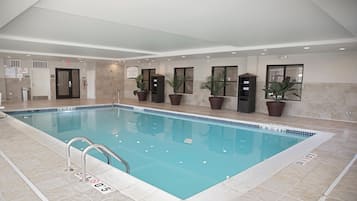 Una piscina interior con agua cristalina, bordes de azulejos y una escalera de metal.