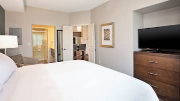 A hotel room with a large bed, a television, a dresser, and a door leading to a bathroom and kitchen.