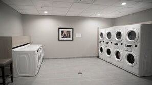 Ein Waschraum mit einer Waschmaschine und einem Trockner, einer Sitzbank und einem gerahmten Bild an der Wand.