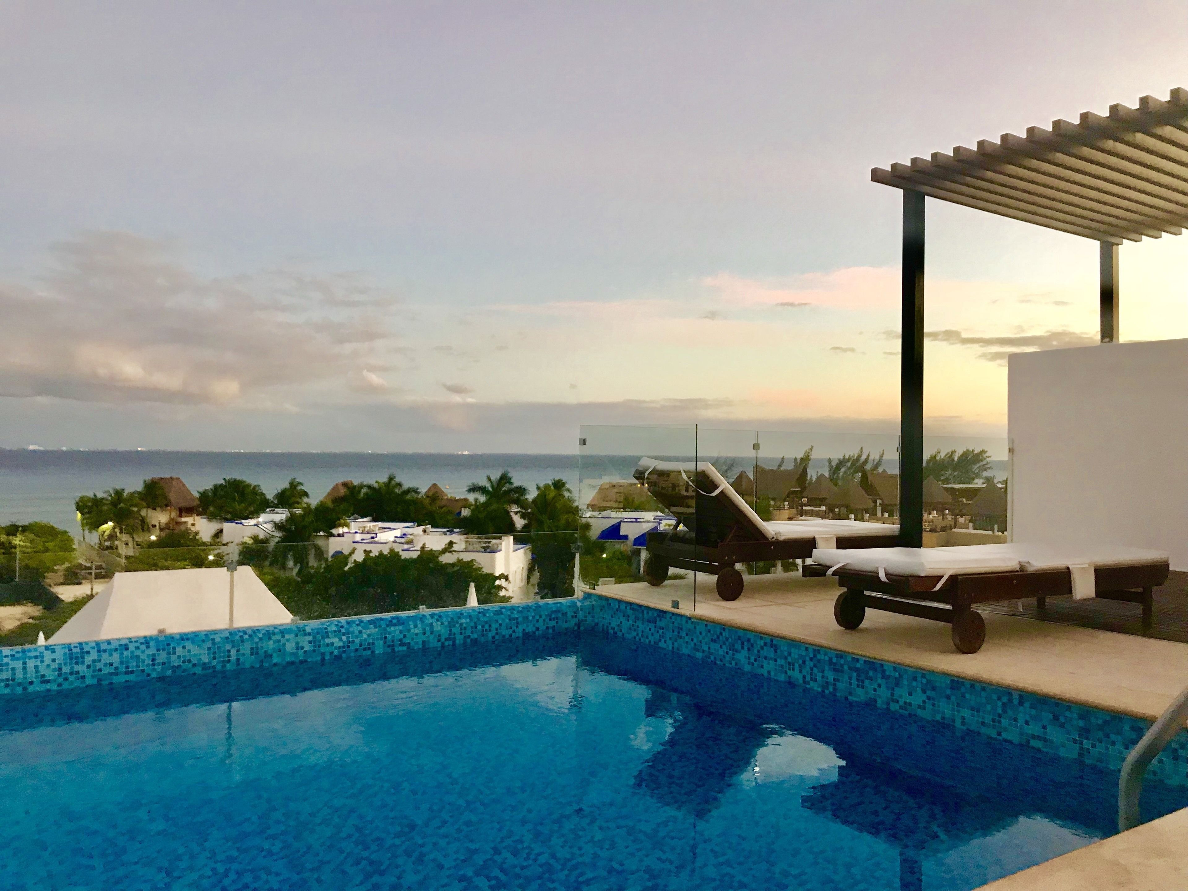 A swimming pool with a view of the ocean and a covered area with lounge chairs.