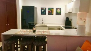 Une cuisine compacte dotée d’un îlot central, de tabourets de bar, d’un réfrigérateur et d’une machine à café.