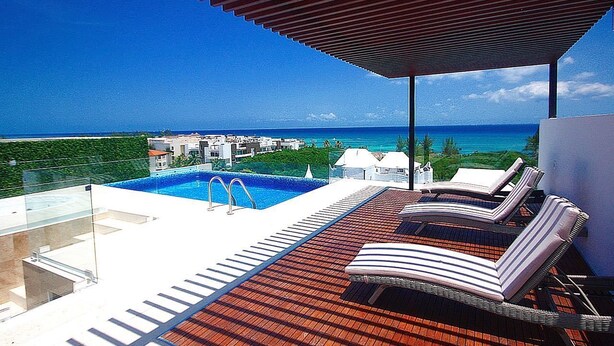 Un espace piscine aménagé sur le toit, avec des chaises longues et une vue dégagée sur l’océan.