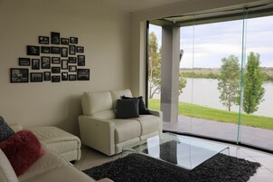 A modern living room with a glass coffee table, a white sofa with a red throw pillow, and a wall of black and white photographs.