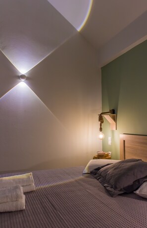 A bedroom with a bed, pillows, a bedside table, and a wall-mounted light fixture.