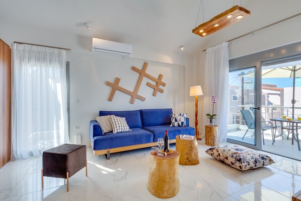A modern living room with a blue sofa, wooden coffee table, and a glass door leading to an outdoor area.
