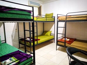 A dormitory room with bunk beds, a chair, and a window with an air conditioning unit.