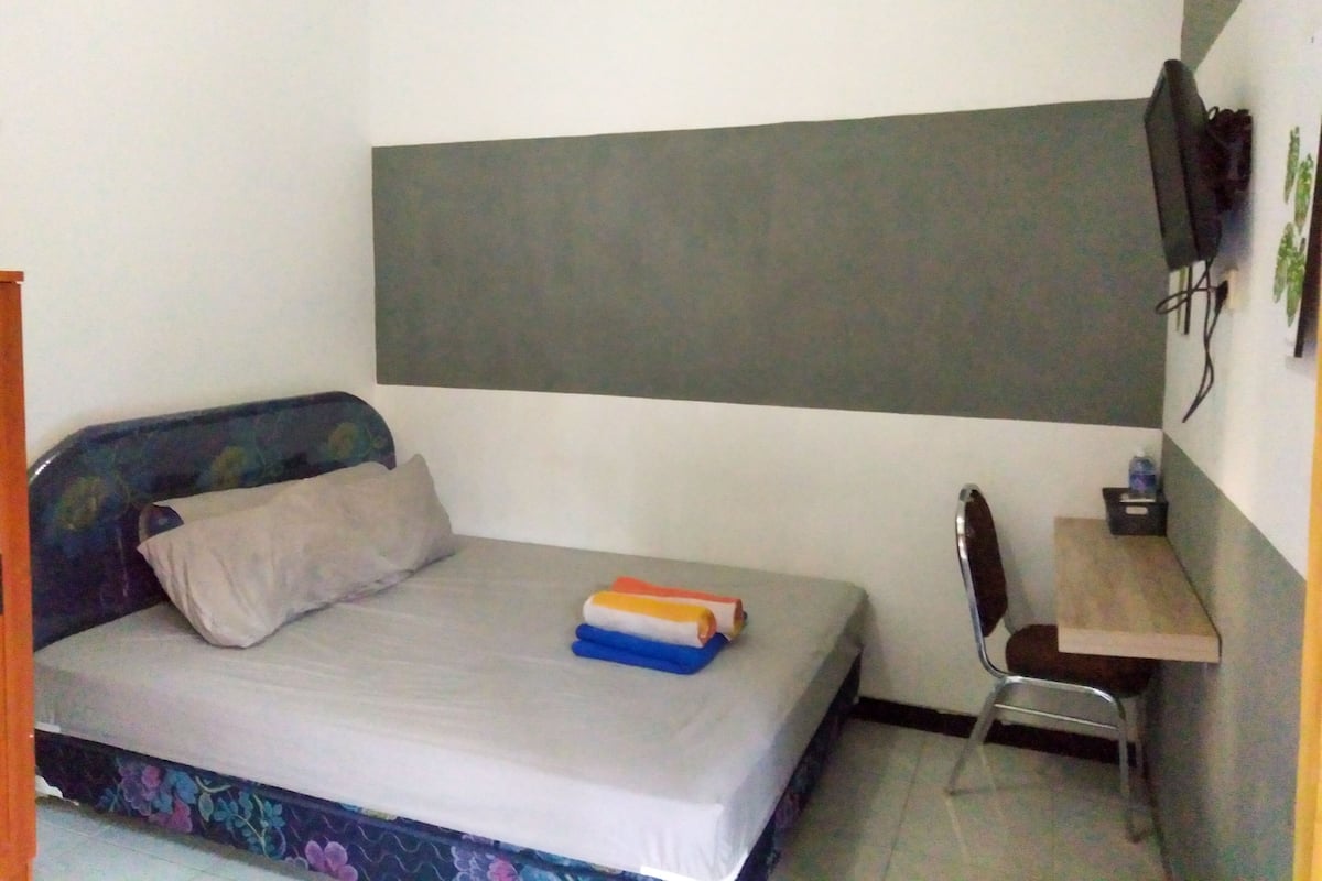 A small, simple room with a bed, a desk, and a chair.