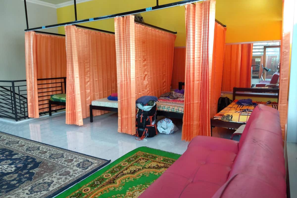 A room with two beds, a sofa, a desk, and orange curtains.