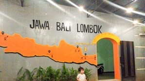 A child standing in front of a wall with a map and text reading "JAWA BALI LOMBOK".
