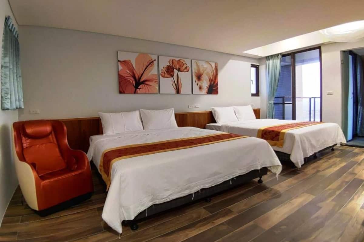A hotel room with two beds, a massage chair, and a large window.
