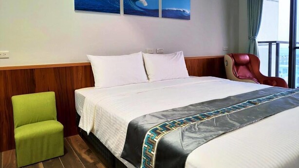 Una camera d'albergo con un letto, una poltrona verde, una poltrona rossa e una finestra vista mare.