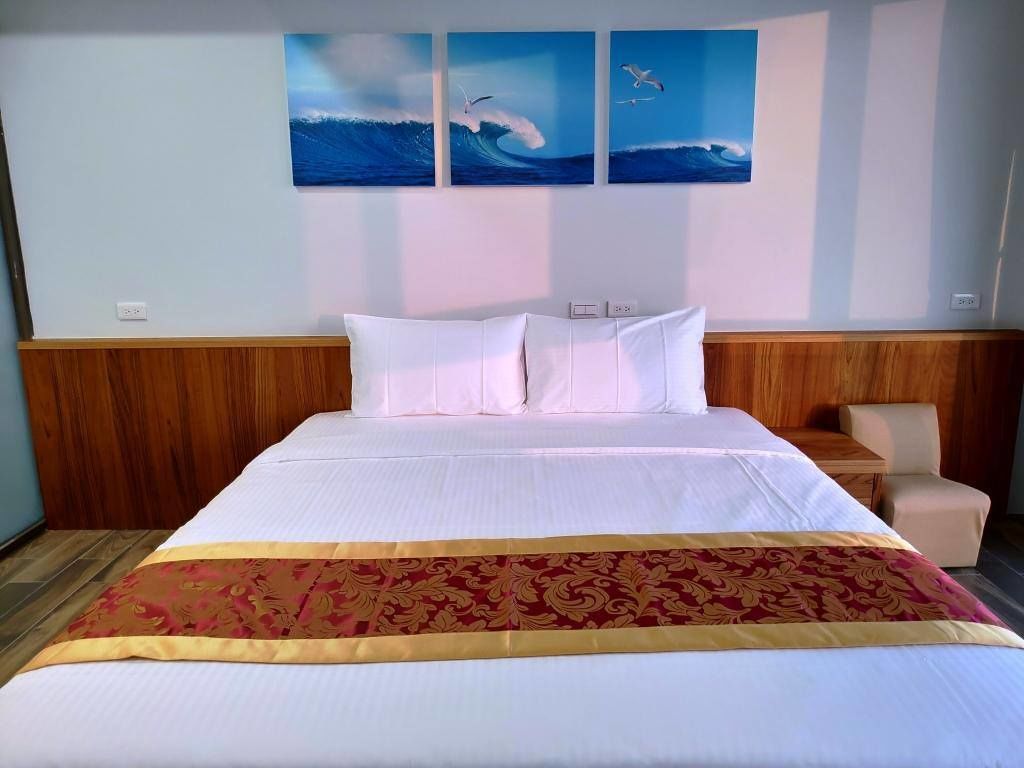 A hotel room with a large bed, a wooden headboard, a bedside table, and a chair. There are three wall-mounted paintings of seagulls and waves.