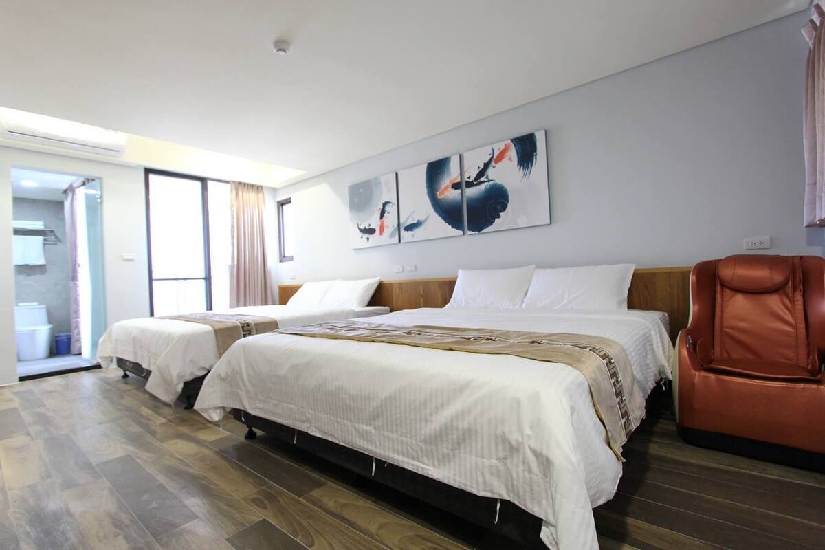 A hotel room with two beds, a massage chair, and artwork on the wall.