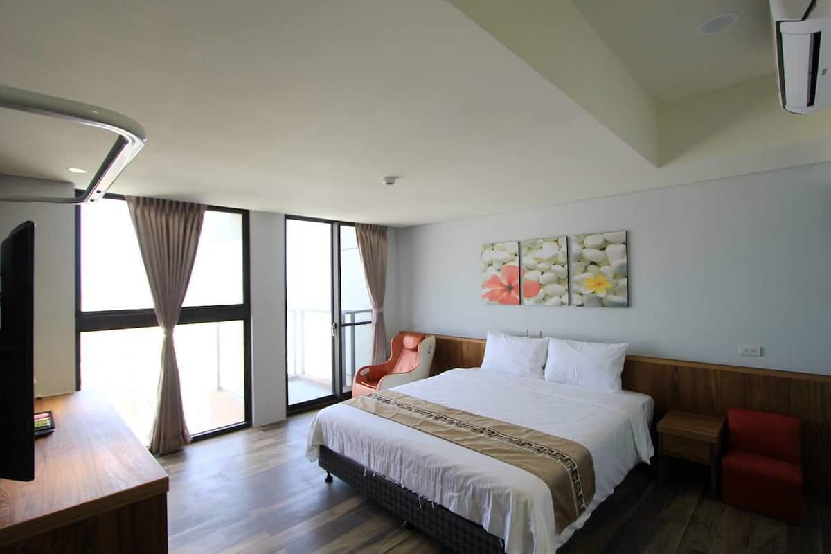 A modern hotel room with a large bed, a desk, a chair, and a large window with curtains.