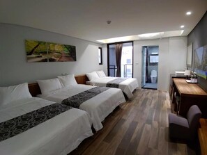 A hotel room with two beds, a desk, and a chair. There is a painting on the wall and a view of the outside.