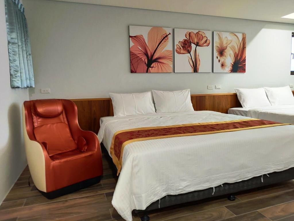 A hotel room with a bed, a massage chair, and three floral wall art pieces.