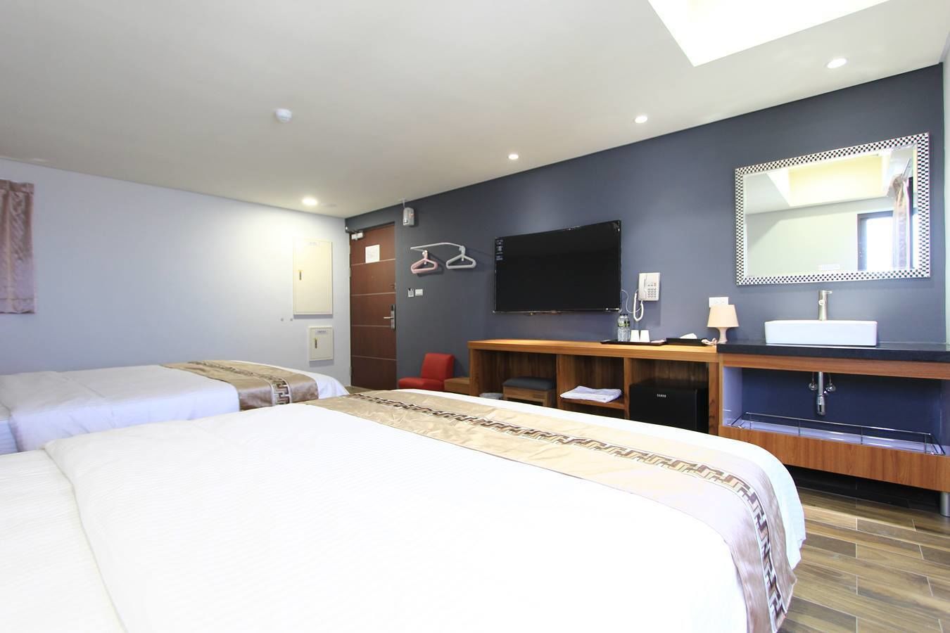 A hotel room with two beds, a desk with a computer, a mirror, and a TV.