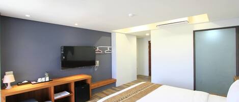 Habitación de hotel con cama, televisor montado en la pared, escritorio con silla y un cesto de basura pequeño.