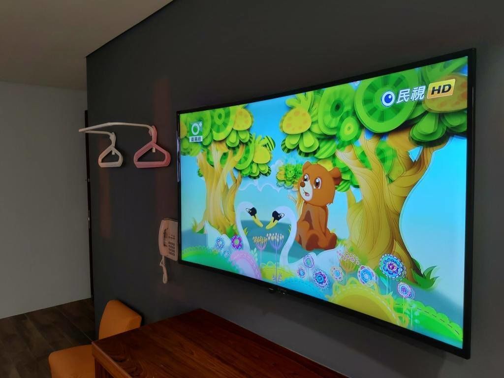 Televisor de pantalla plana montado en una pared mostrando una escena animada y colorida con árboles y animales.