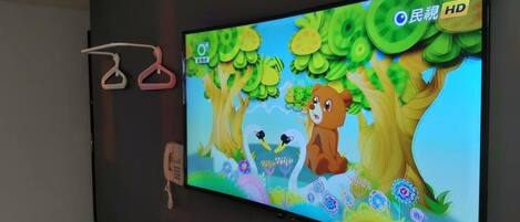 Televisor de pantalla plana montado en una pared mostrando una escena animada y colorida con árboles y animales.