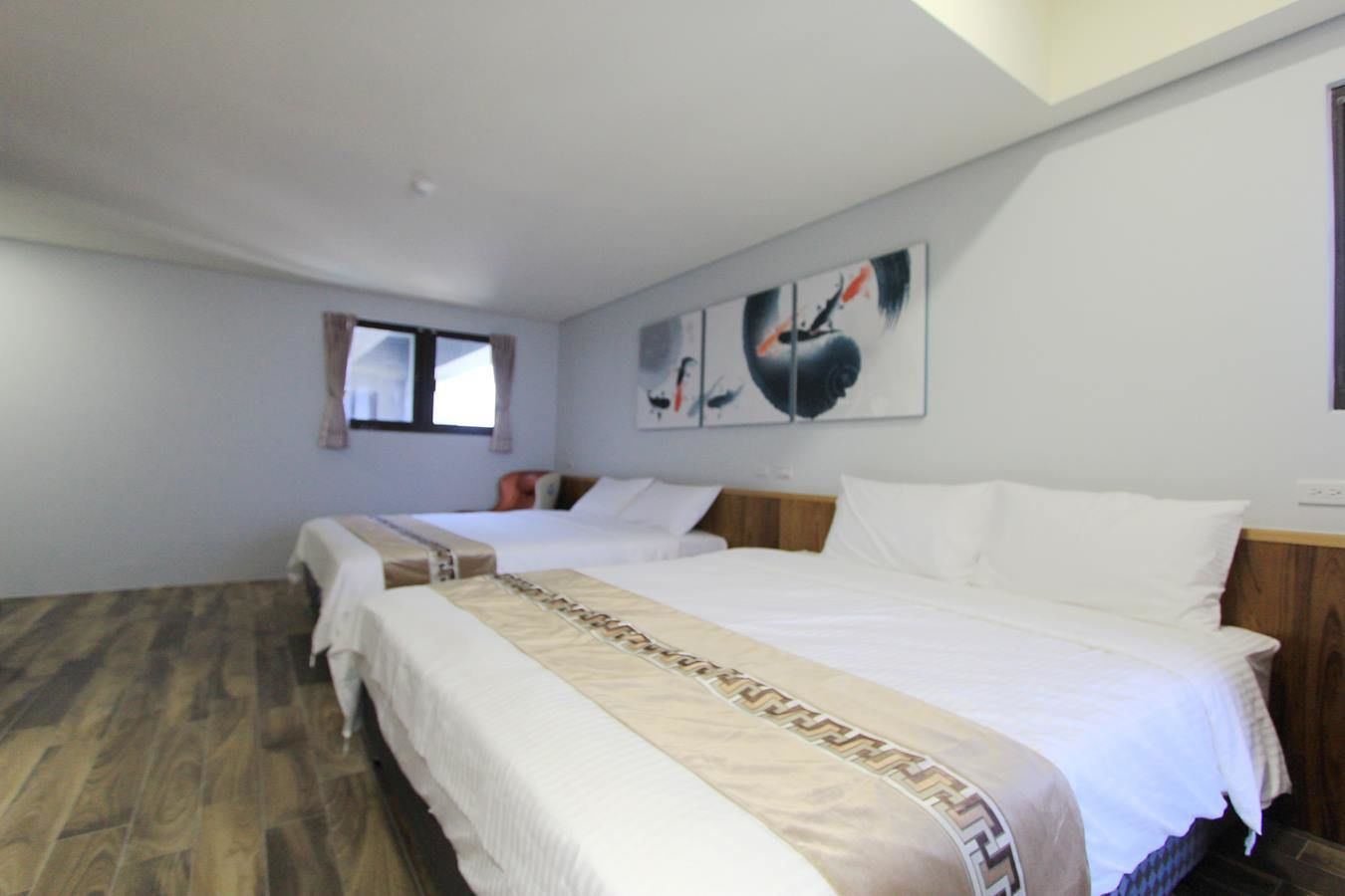Una habitación de hotel con dos camas, suelo de madera y obras de arte en las paredes.