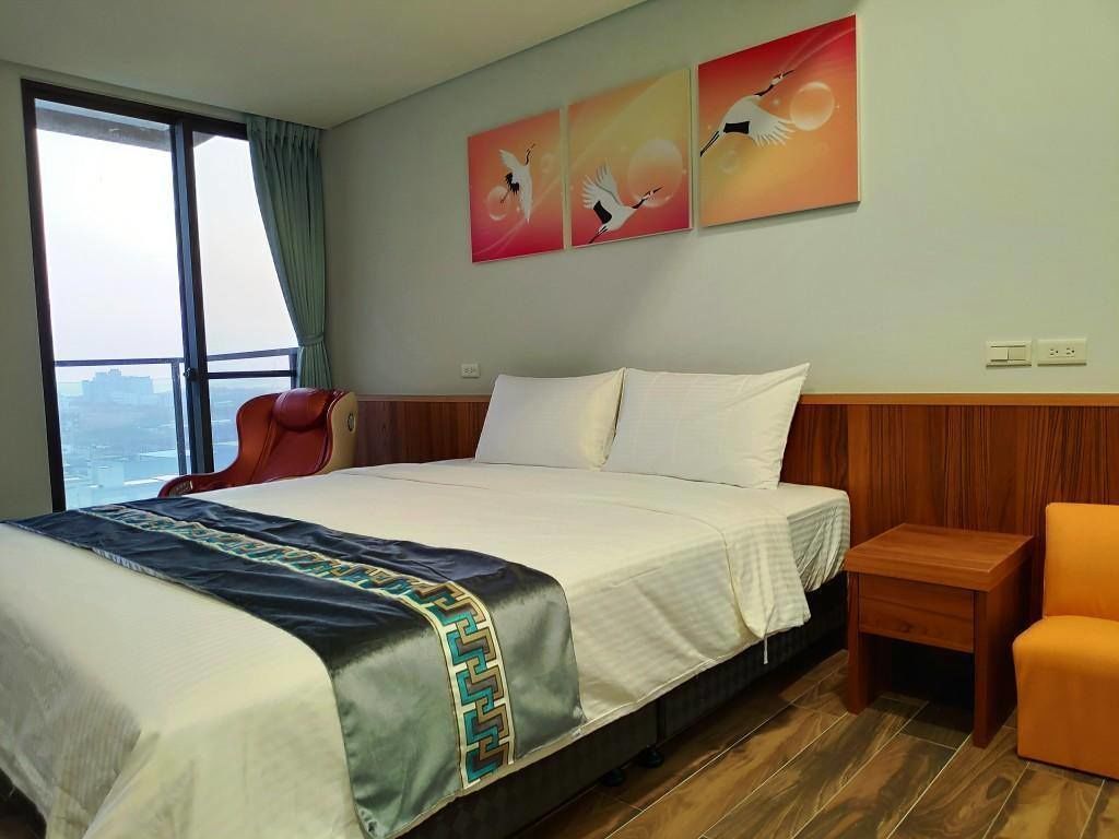 Ein Hotelzimmer mit einem großen Bett, einem Holzkopfteil, einem Nachttisch, einem orangefarbenen Sessel und einem Fenster mit Blick auf die Stadt.