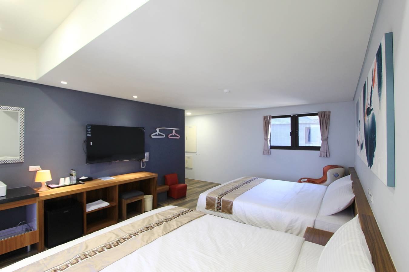 A hotel room with two beds, a desk, a TV, and a window with curtains.