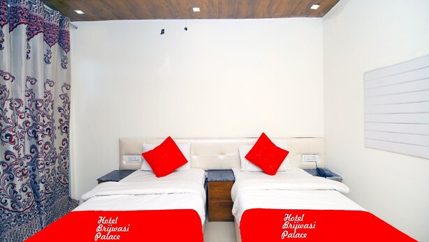 A hotel room with two beds, red pillows, a wooden headboard, and a patterned curtain. - Hotel brijwasi palace (Yamkeshwar)